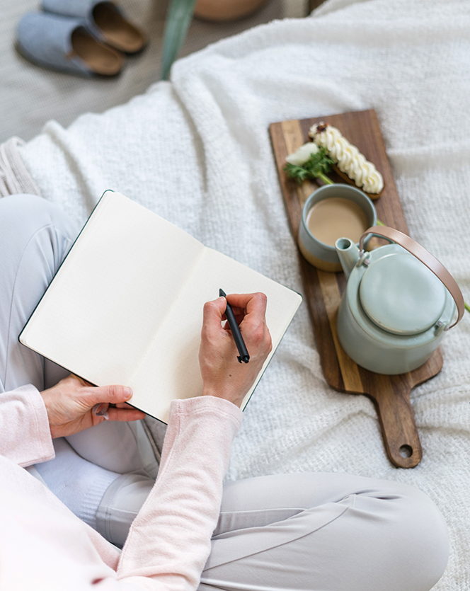 Top vertical view of student woman sit on bed in boho chic bedroom, make education notes in journal, study at home. Inspiration concept. Female hands hold pen and personal diary with copy space pages